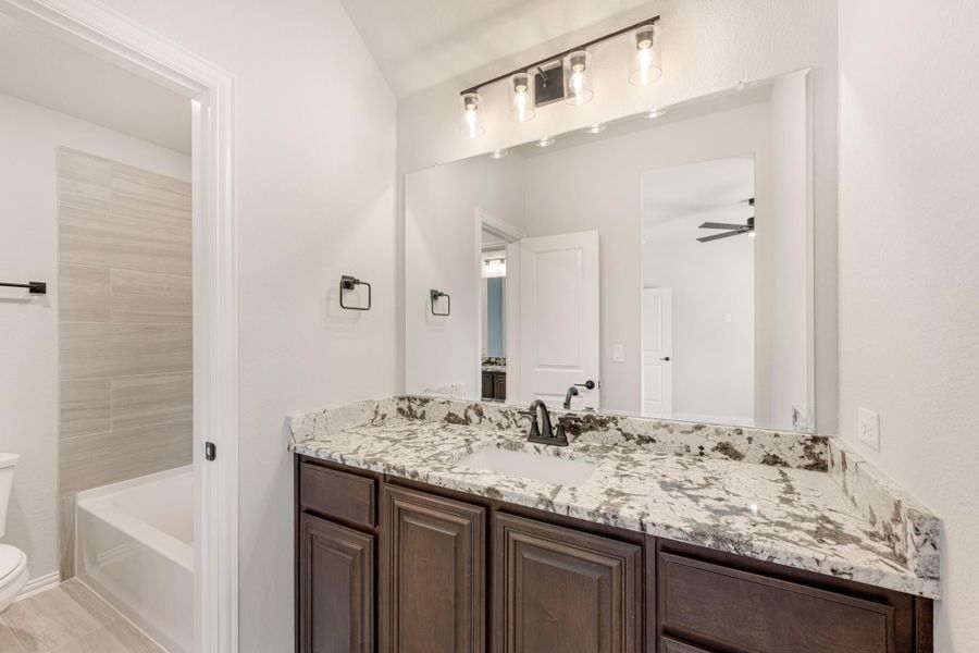 Bathroom with dark wood vanity, granite countertop, large mirror, and tiled soaking tub with shower combo Bathroom with dark wood vanity, granite countertop, large mirror, and tiled soaking tub with shower combo