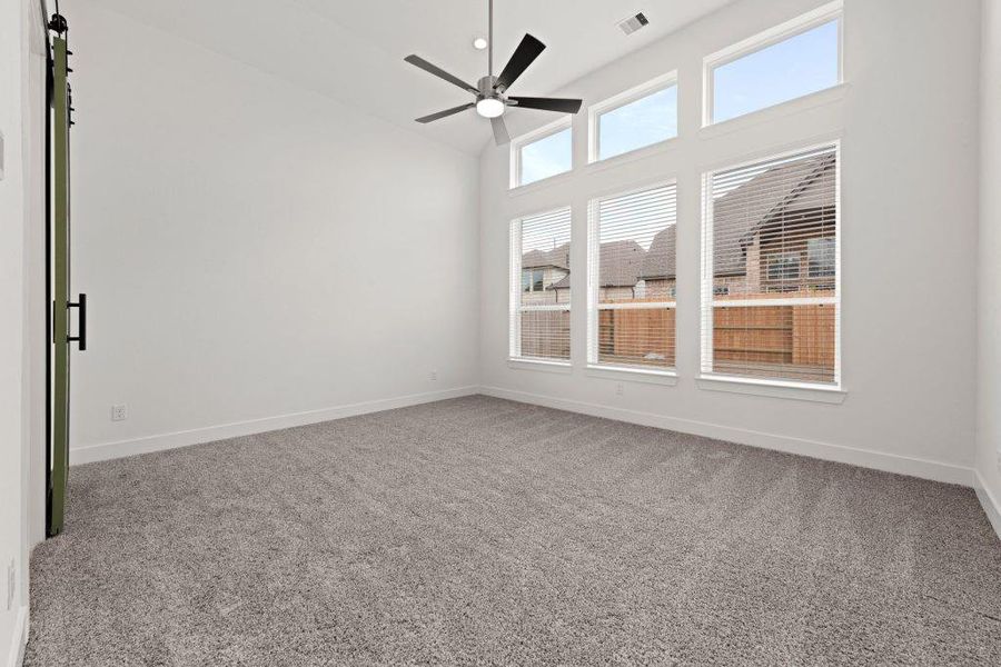 A spacious room features a sleek ceiling fan and an abundance of natural light from large windows.