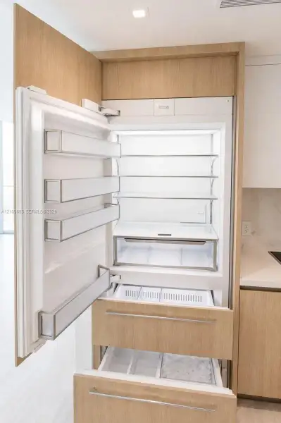 Integrated refrigerator featuring custom wood-finish cabinetry panels, adjustable shelving, tiered pull-out freezer drawers, and recessed lighting