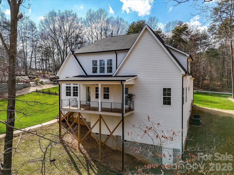 Rear exterior view showcasing the home’s elevated covered deck and peaceful wooded lakefront setting.