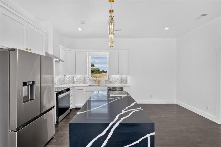 Kitchen featuring a dark, veined island, white cabinetry, stainless steel appliances, herringbone tile backsplash, and wood-finish flooring