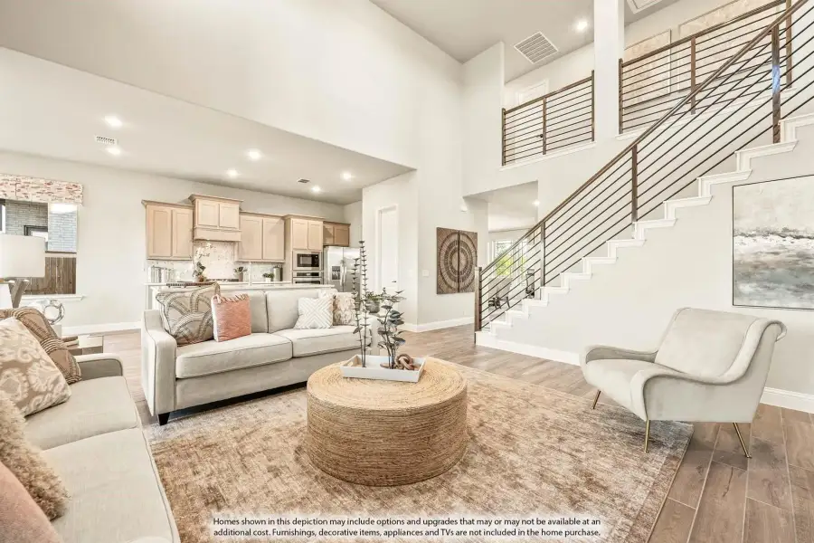 Open living room with two-story ceiling, staircase, hardwood floors, and open kitchen in background