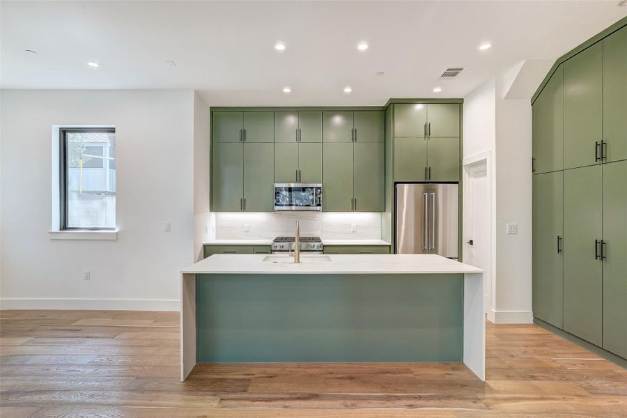 Kitchen with green cabinetry, stainless steel appliances, tasteful backsplash, an island with sink, and recessed lighting