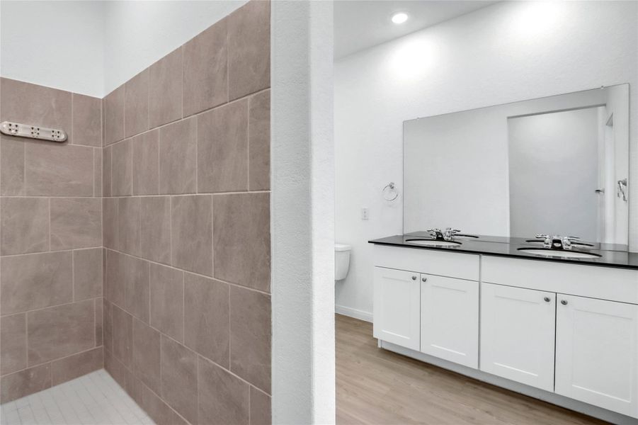 Bathroom featuring double vanity, light wood-style floors, and a tile shower