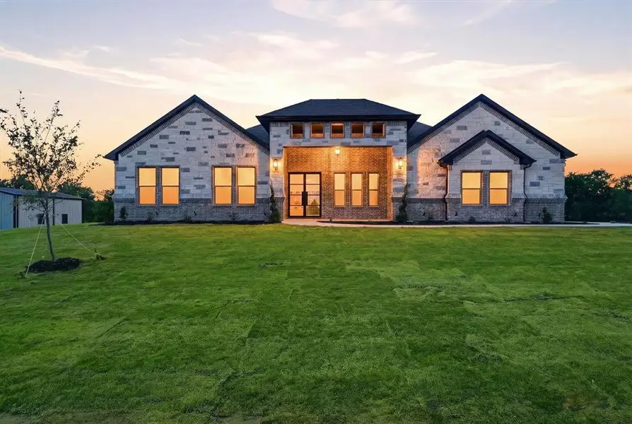 Back of house at dusk with a yard, brick siding, and stone siding