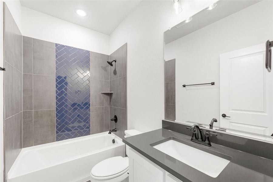 Bathroom with tiled tub-shower combo featuring blue herringbone accent tile, gray countertop vanity, and white cabinets