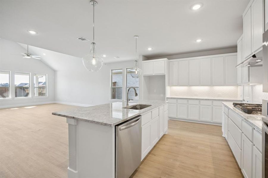 Kitchen featuring tasteful backsplash, white cabinets, stainless steel appliances, light stone counters, and hanging light fixtures