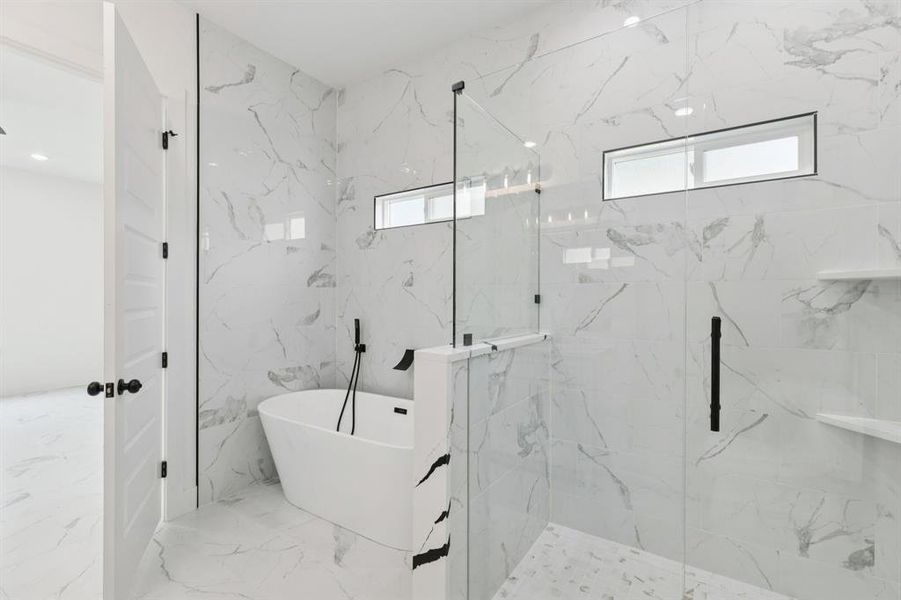 Full bath featuring healthy amount of natural light, a freestanding tub, marble tiled flooring, and a marble finish shower