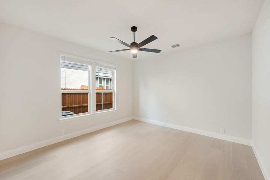 Empty bedroom with light hardwood floors, black ceiling fan, and double windows with white trim Empty bedroom with light hardwood floors, black ceiling fan, and double windows with white trim