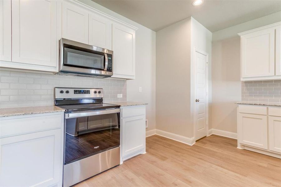 Kitchen with white cabinets, decorative backsplash, stainless steel appliances, light stone countertops, and light hardwood / wood-style flooring Kitchen with white cabinets, decorative backsplash, stainless steel appliances, light stone countertops, and light hardwood / wood-style flooring