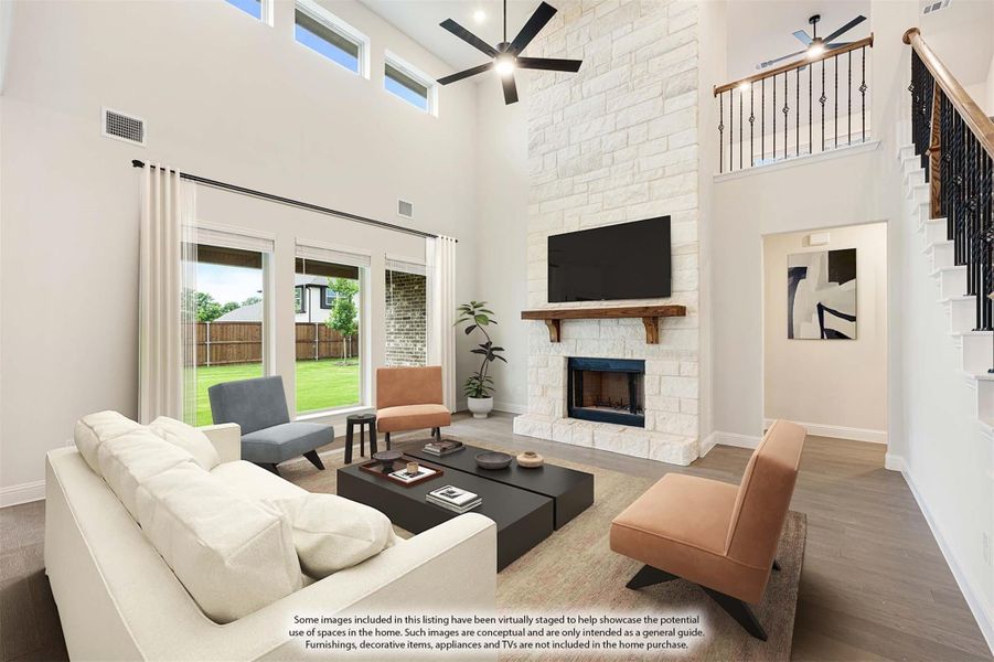 Living room with two-story ceiling, stone fireplace, ceiling fan, and hardwood floors next to a staircase Living room with two-story ceiling, stone fireplace, ceiling fan, and hardwood floors next to a staircase