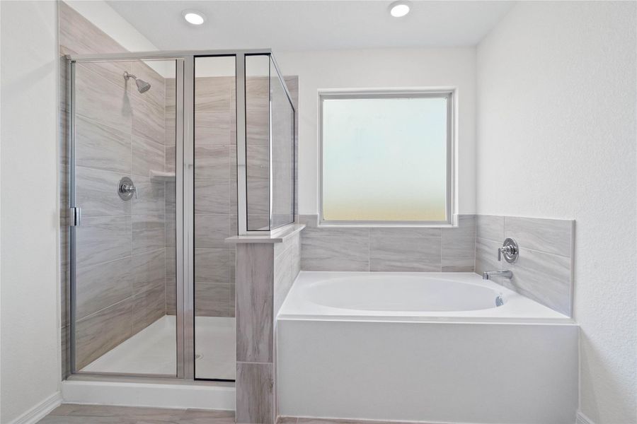 This additional view of the primary bath highlights a walk-in shower with elegant tile surround, a separate garden tub ideal for relaxing after a long day, and a large rain glass window that offers both natural light and privacy. This additional view of the primary bath highlights a walk-in shower with elegant tile surround, a separate garden tub ideal for relaxing after a long day, and a large rain glass window that offers both natural light and privacy.