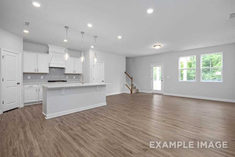 Kitchen with decorative backsplash, decorative light fixtures, hardwood / wood-style floors, white cabinetry, and an island with sink