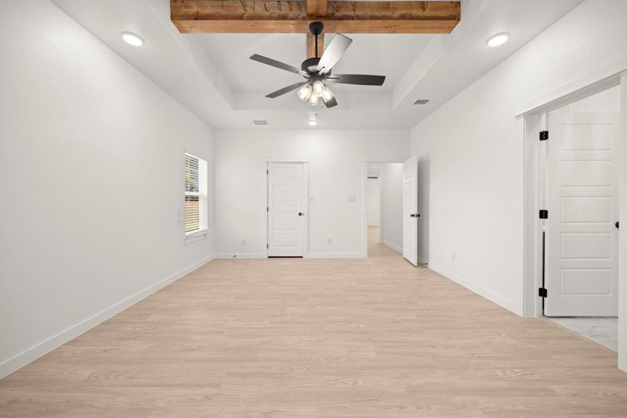 A clean, airy primary bedroom offers light wood flooring and a classic ceiling fan for ultimate comfort.