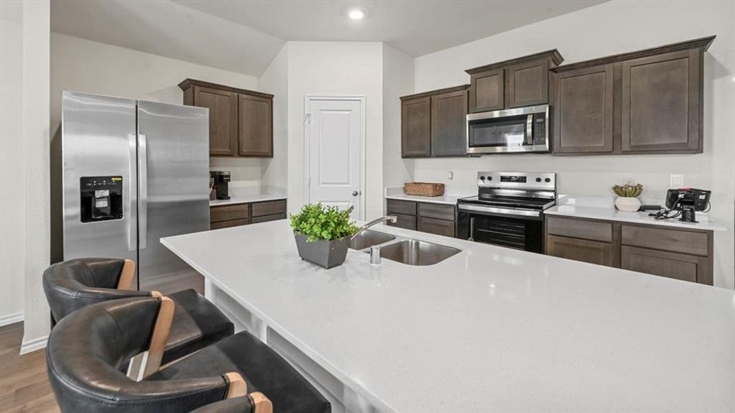 Kitchen with appliances with stainless steel finishes, dark brown cabinets, a kitchen bar, light stone counters, and dark wood-type flooring Kitchen with appliances with stainless steel finishes, dark brown cabinets, a kitchen bar, light stone counters, and dark wood-type flooring