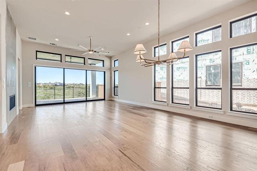 Unfurnished living room with ceiling fan with notable chandelier, plenty of natural light, and light hardwood / wood-style flooring