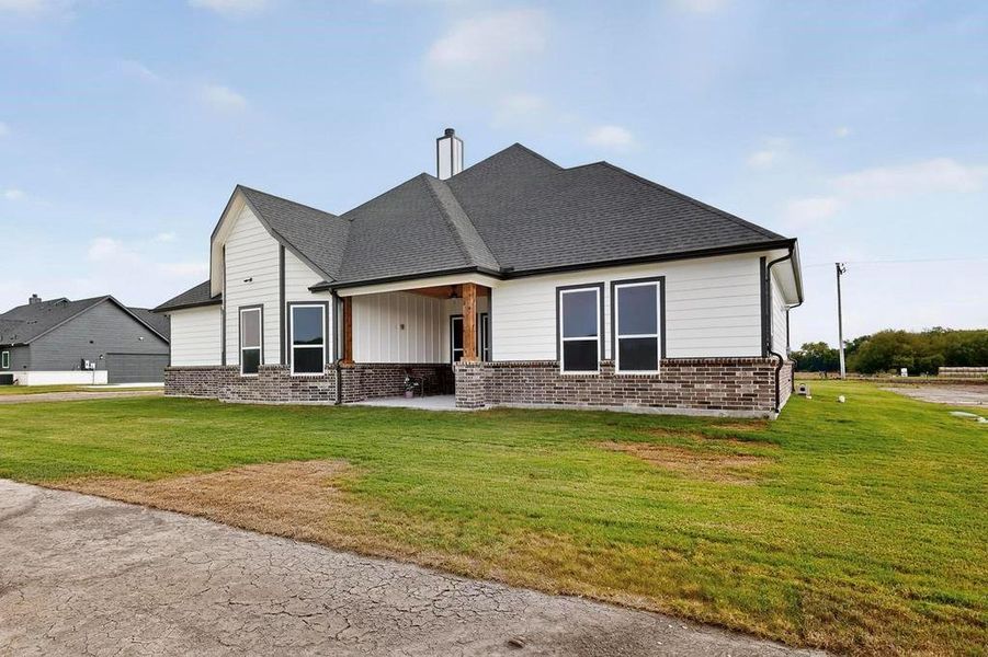 View of front facade featuring a patio area, roof with shingles, a front yard, and brick siding View of front facade featuring a patio area, roof with shingles, a front yard, and brick siding