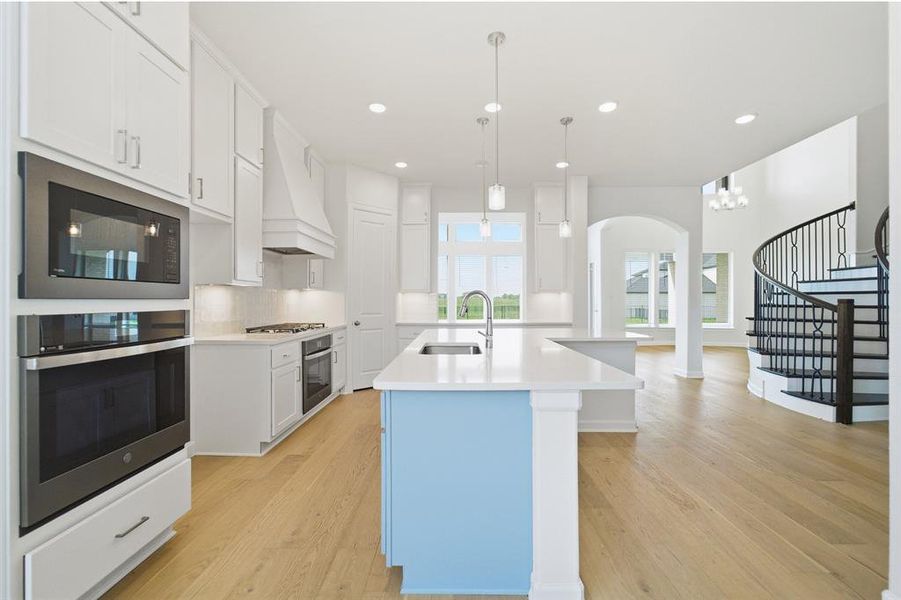 Open-concept kitchen featuring a light blue island with a white countertop, stainless steel appliances, white cabinetry, and wood-finish flooring