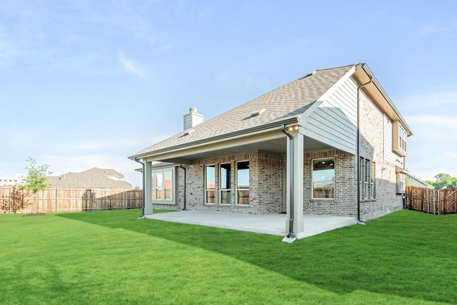 Rear view of two-story brick home with covered patio, green lawn, and wood privacy fence