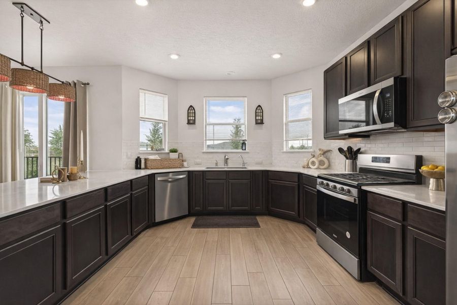 Bright U-shaped kitchen with sleek dark cabinetry, quartz-style counters, subway tile, and abundant natural light.