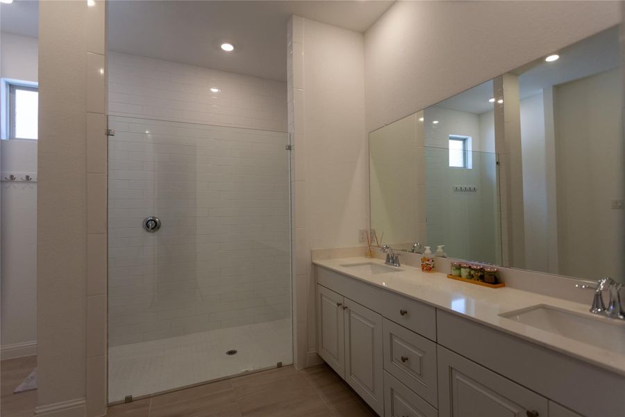 This bathroom features a spacious glass-enclosed shower with white subway tiles and a large double vanity with ample storage. The modern design is complemented by recessed lighting and a neutral color palette.