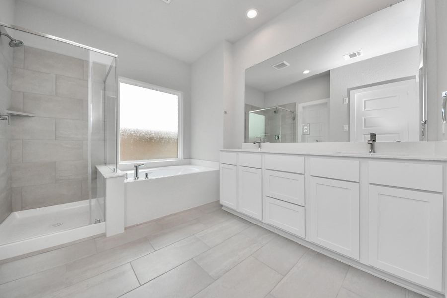 Escape to a spa-like oasis in this primary bathroom. Enjoy a walk-in shower with tile surround, a separate garden tub with custom detailing, and an elegant vanity featuring light countertops, modern hardware, and beautiful vanity lights. Experience luxury and relaxation in every detail. Sample photo of completed home with similar floor plan. Actual colors and selections may vary.