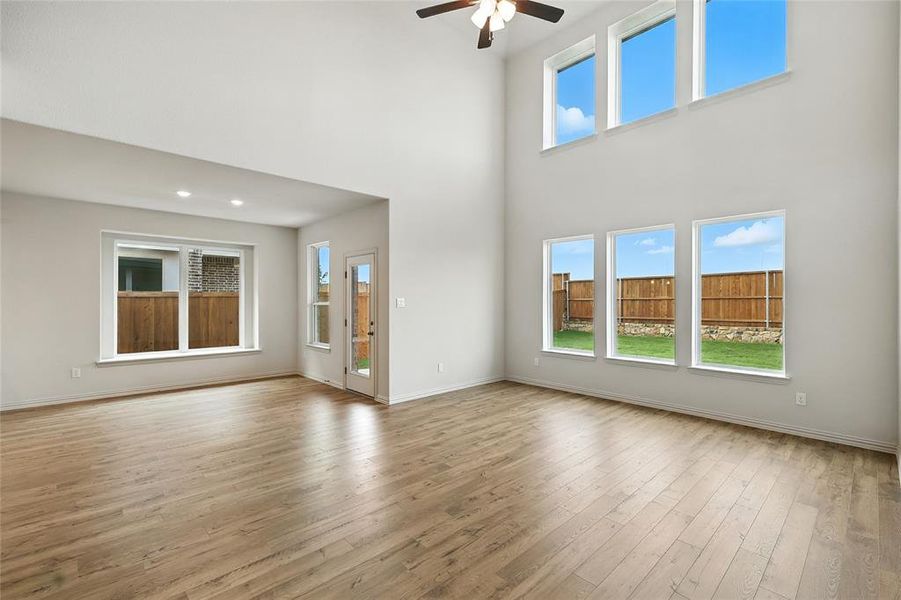 Unfurnished living room featuring light wood-type flooring, a high ceiling, and ceiling fan