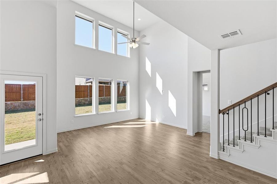 Unfurnished living room with light wood-type flooring, ceiling fan, stairway, and a towering ceiling