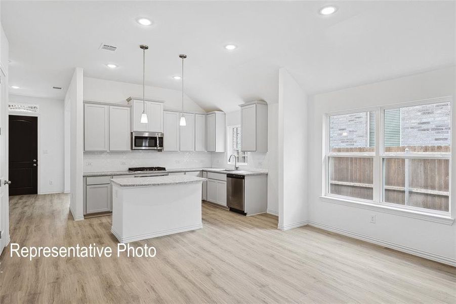Open-concept kitchen and living area featuring wood-finish flooring, recessed lighting, and a vaulted ceiling