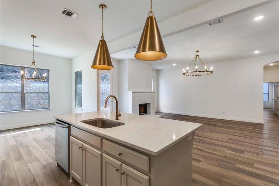 Kitchen featuring sink, hanging light fixtures, dishwasher, light stone countertops, and a kitchen island with sink