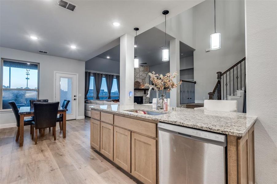Kitchen with dishwasher, light brown cabinetry, light stone counters, light wood-style floors, and open floor plan Kitchen with dishwasher, light brown cabinetry, light stone counters, light wood-style floors, and open floor plan