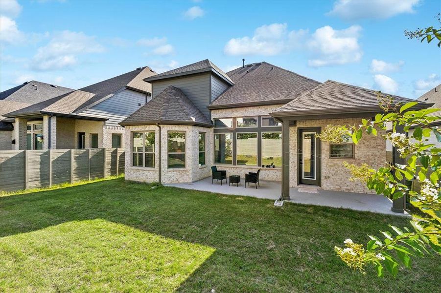 Expansive backyard with a manicured lawn, featuring a covered patio, brick exterior, bay windows, and a privacy fence Expansive backyard with a manicured lawn, featuring a covered patio, brick exterior, bay windows, and a privacy fence