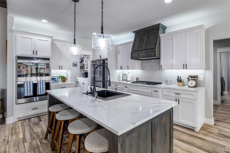 Kitchen featuring pendant lighting, sink, white cabinets, and a center island with sink