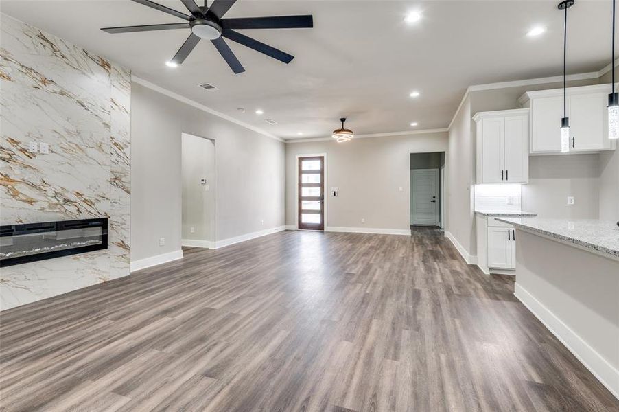 Unfurnished living room with ceiling fan, ornamental molding, recessed lighting, a fireplace, and dark wood-style flooring