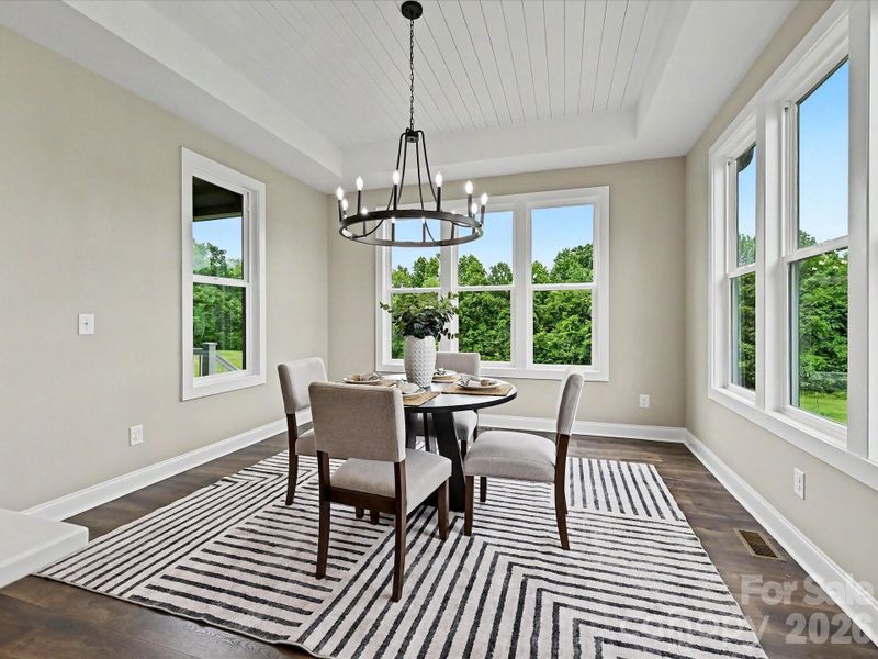 Elegant dining area offers a warm and inviting space to gather, highlighted by designer lighting, tray ceiling detail, and seamless flow into the gourmet kitchen.