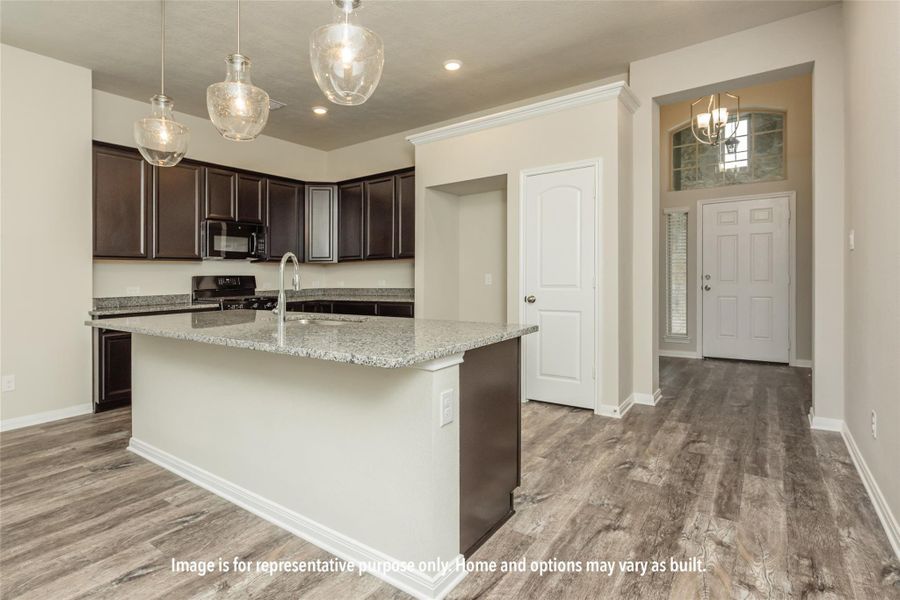 Kitchen with dark wood finish cabinetry, light stone counters, black appliances, a kitchen island with sink, and light wood-style floors