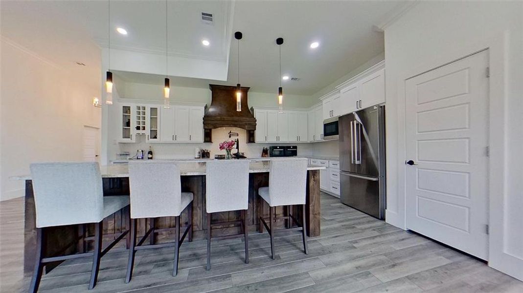 Spacious kitchen featuring an expansive center island, white cabinetry, stainless steel appliances, a decorative wood range hood, and tile flooring Spacious kitchen featuring an expansive center island, white cabinetry, stainless steel appliances, a decorative wood range hood, and tile flooring