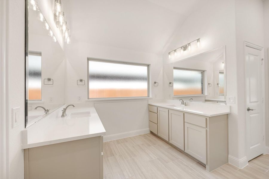 Dual-vanity master bathroom with white countertops, gray cabinets, vaulted ceiling, and frosted windows