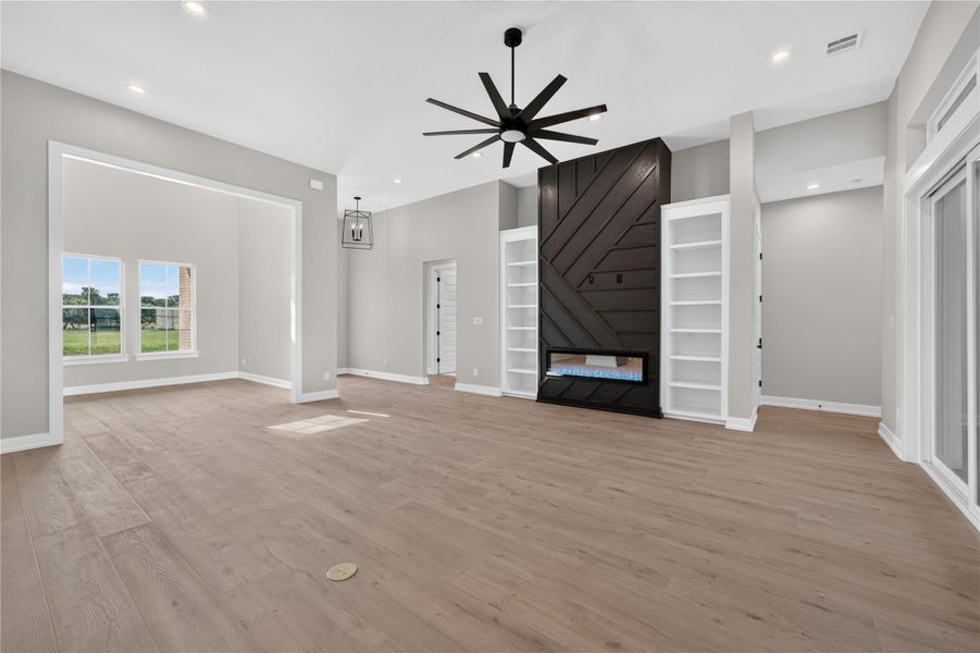 An open floorplan showcases smooth wood flooring, high ceilings, and a modern focal fireplace.