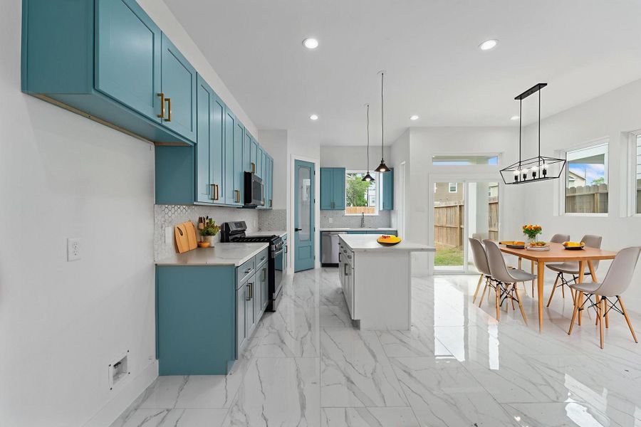 Modern open-concept kitchen and dining area featuring vibrant blue cabinetry, elegant gold-tone accents, and sleek marble-style flooring.