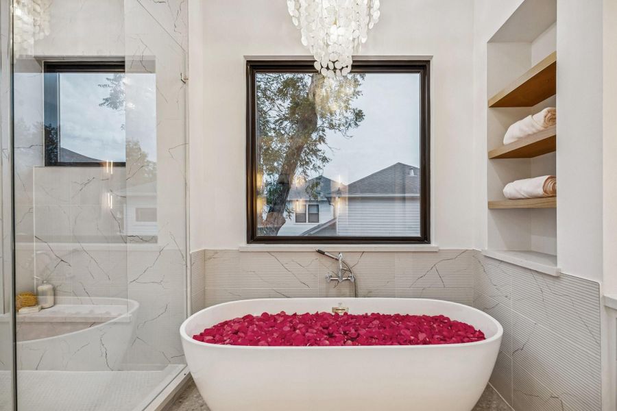 71 Inch Soaking Tub with a Wall Mounted Tub Filler, Ribbed Marble Tile Tub Surround, GlossyBronze Tiered Chandelier with Natural White Shell, White Oak Floating Shelves with a Natural Stain.