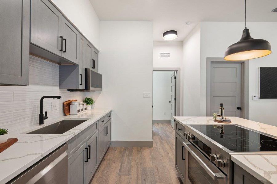 Kitchen with light stone countertops, stainless steel appliances, hanging light fixtures, light wood-type flooring, and gray cabinets