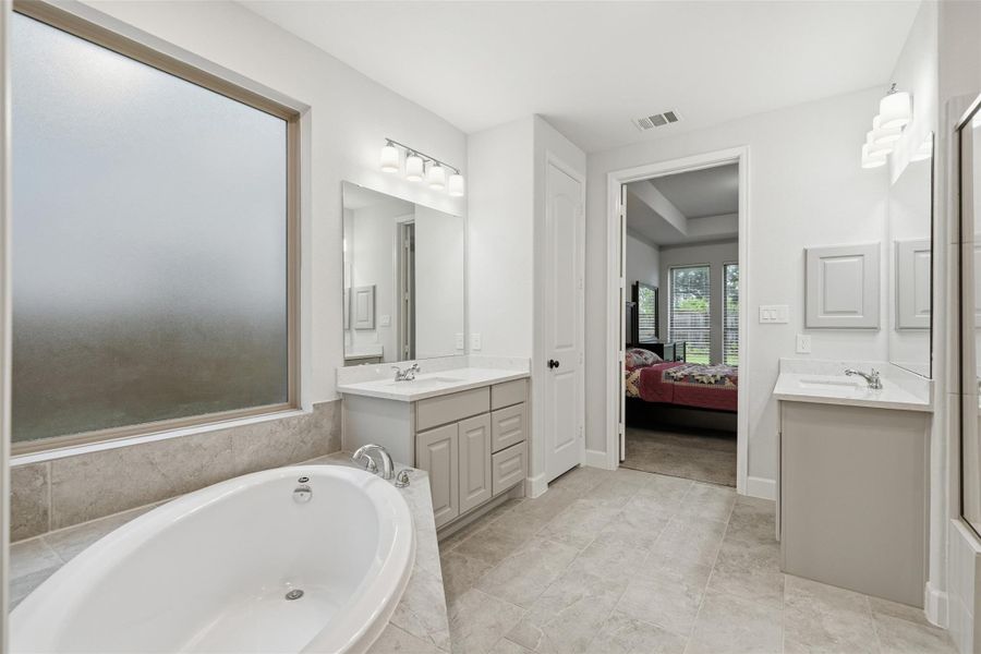 This modern bathroom features a spacious bathtub, dual vanities with ample storage, and a large frosted window for natural light. The neutral tile flooring and contemporary fixtures create a clean, inviting atmosphere. This modern bathroom features a spacious bathtub, dual vanities with ample storage, and a large frosted window for natural light. The neutral tile flooring and contemporary fixtures create a clean, inviting atmosphere.