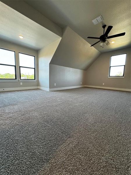 Additional living space with a textured ceiling, carpet flooring, vaulted ceiling, and ceiling fan