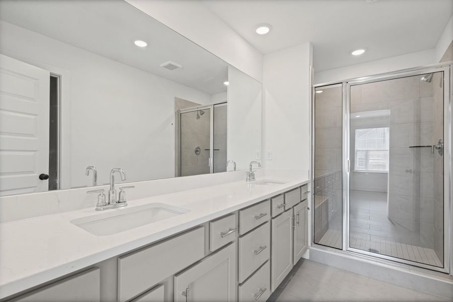 Double vanity with a white countertop and undermount sinks, custom cabinetry, a wall-mounted mirror, and a glass-enclosed shower with a built-in bench