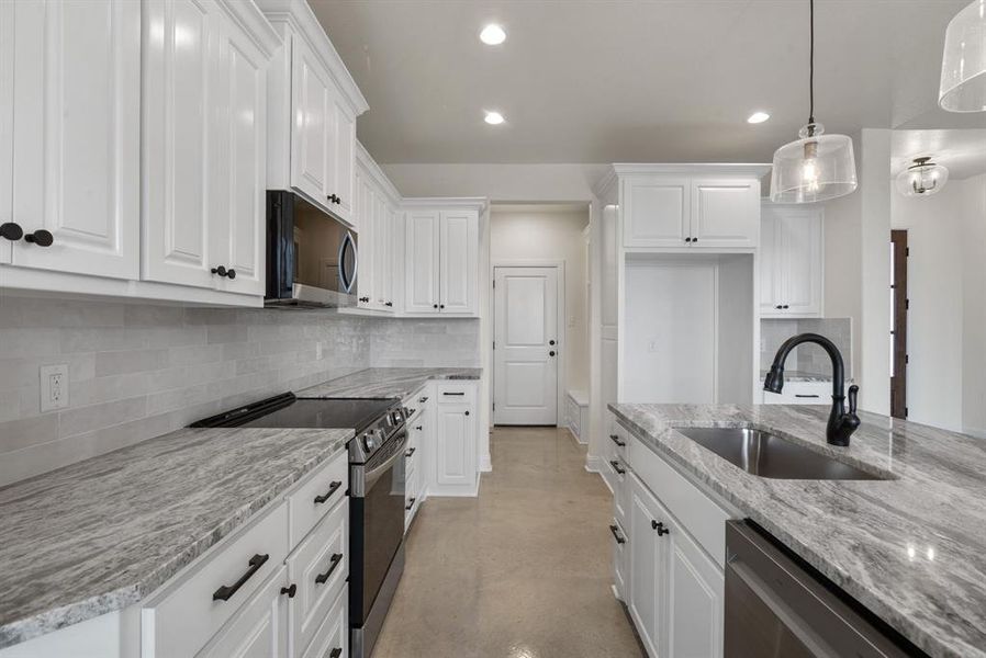 Kitchen featuring stainless steel appliances, light stone counters, pendant lighting, sink, and white cabinetry