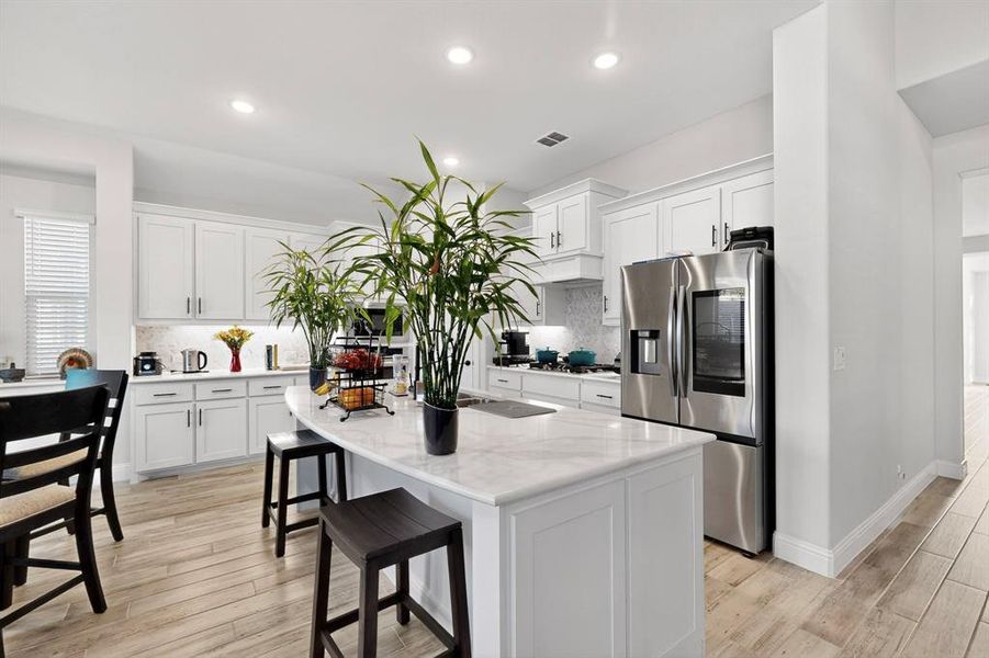 Kitchen featuring backsplash, a breakfast bar, stainless steel fridge, white cabinets, and light wood-style floors Kitchen featuring backsplash, a breakfast bar, stainless steel fridge, white cabinets, and light wood-style floors