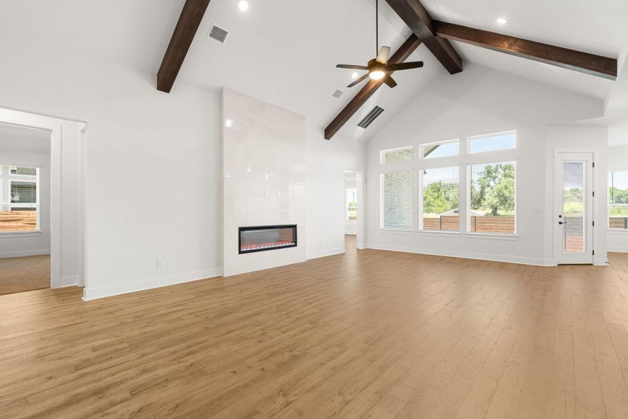 A spacious living room features soaring vaulted ceilings, natural wood beams, and an elegant fireplace.