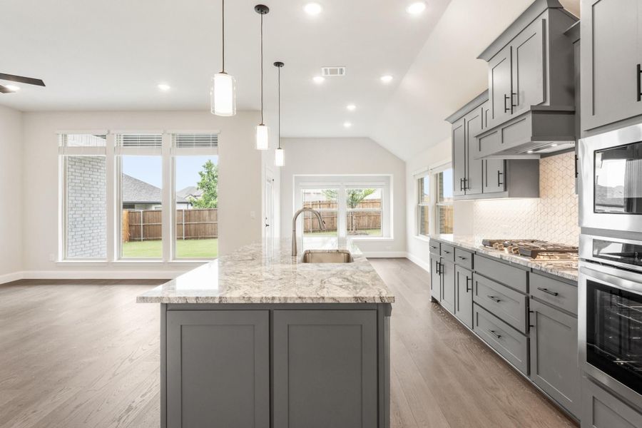Kitchen with gray cabinets, large granite island, pendant lights, and stainless steel appliances on hardwood floors Kitchen with gray cabinets, large granite island, pendant lights, and stainless steel appliances on hardwood floors