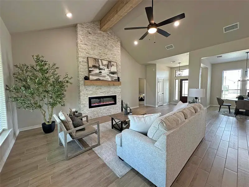 Living room with light wood-type flooring, beam ceiling, a ceiling fan, high vaulted ceiling, and a fireplace Living room with light wood-type flooring, beam ceiling, a ceiling fan, high vaulted ceiling, and a fireplace